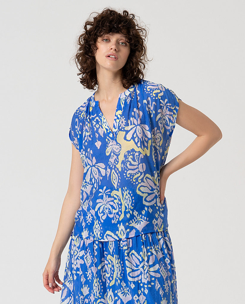 Woman wearing a blue floral top & skirt against a plain background