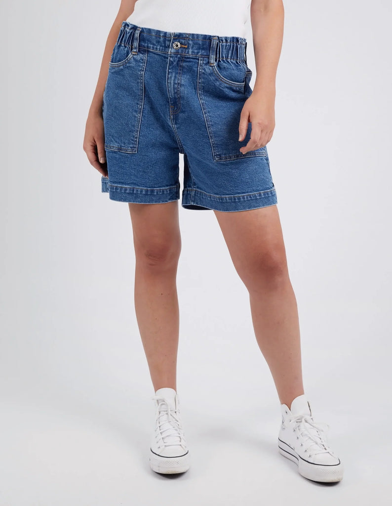 Person wearing elm blue denim shorts and white sneakers on a white background