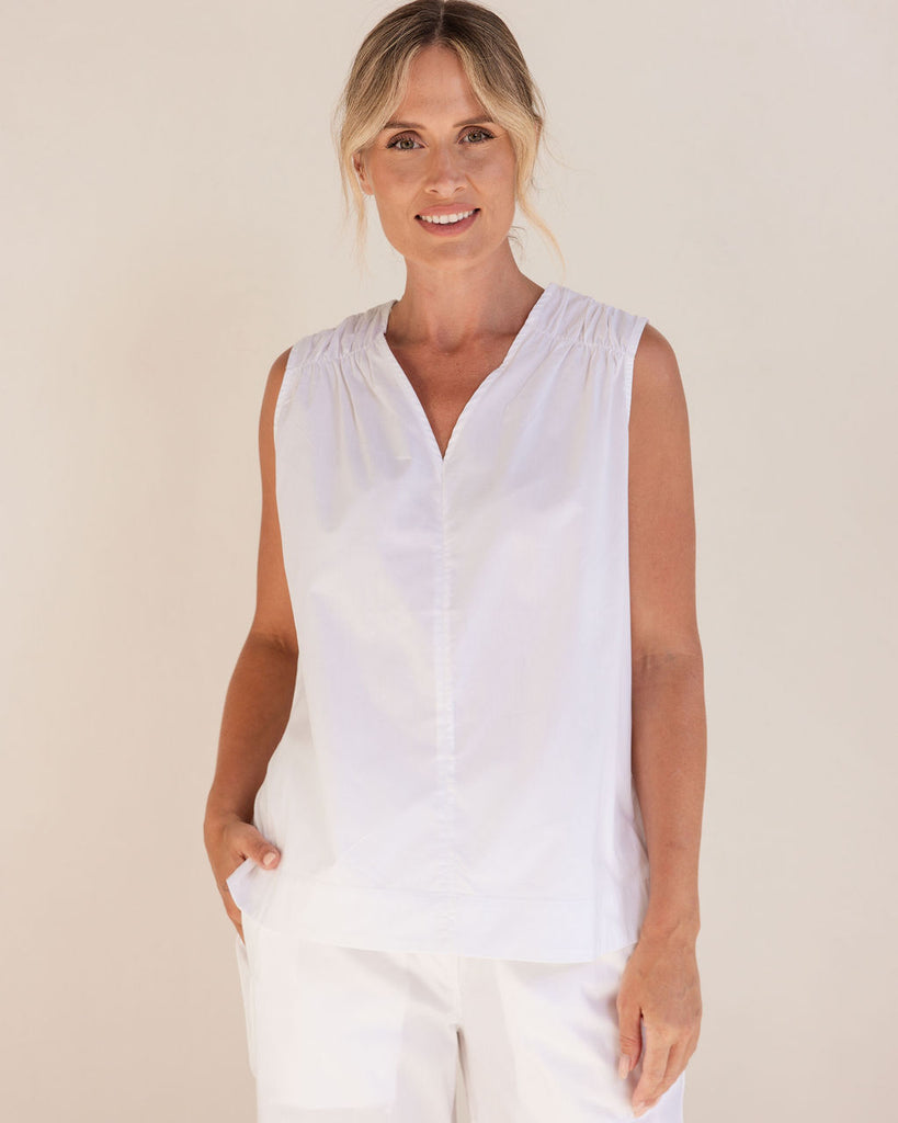 Woman wearing a See Saw white sleeveless top and pants against a plain background