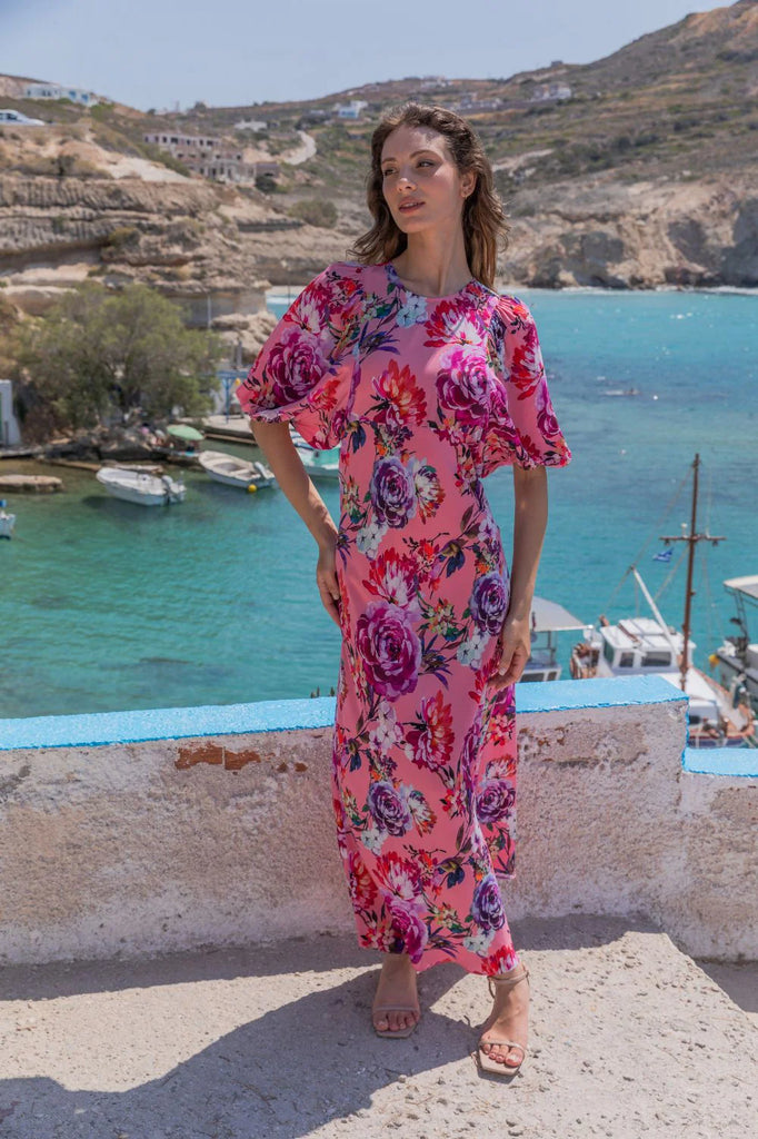 Woman in a Kachel floral dress standing by a scenic coastal view with boats and mountains.
