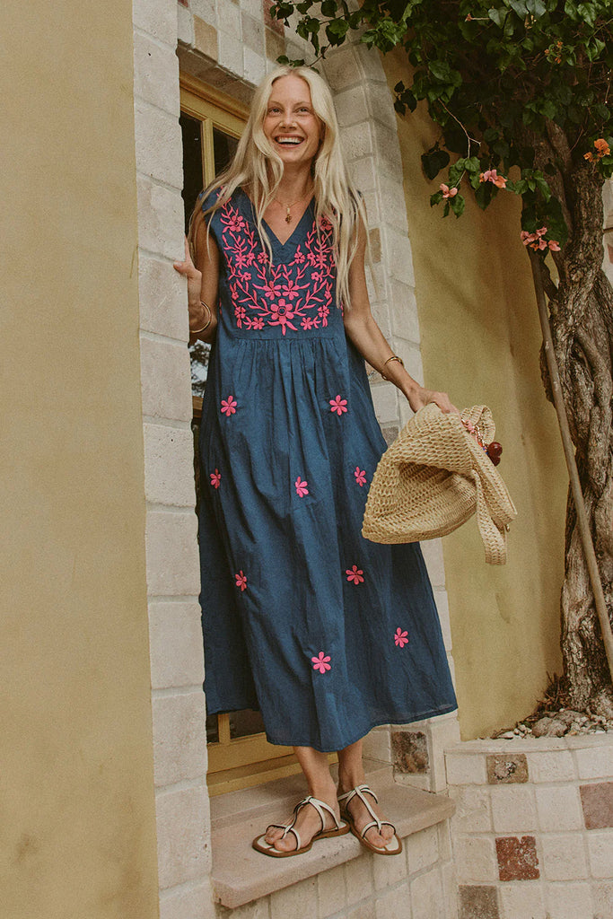 Woman in a Rubyyaya Andaman blue dress with pink floral embroidery standing outside a building.